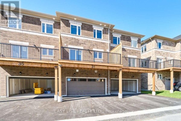 Rear view of townhouses showing garages, decks, and balconies under a sunny sky. - 31 Addyman Crescent, Clarington
