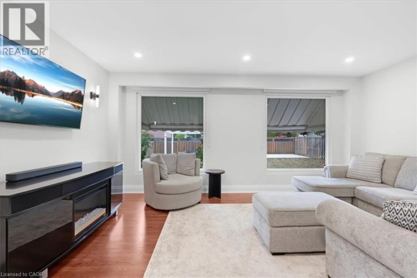Living room with sectional sofa, swivel chair, large TV, electric fireplace, and backyard view. - 31 Berrisfield Crescent, Hamilton