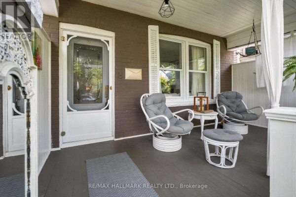 Covered front porch with white wicker furniture and a glass-paneled front door. - 31 Cassels Avenue, Toronto