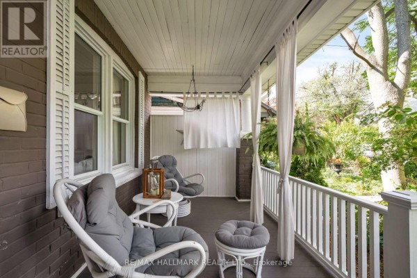 Close-up of a front porch with seating, white railing, and sheer curtains. - 31 Cassels Avenue, Toronto