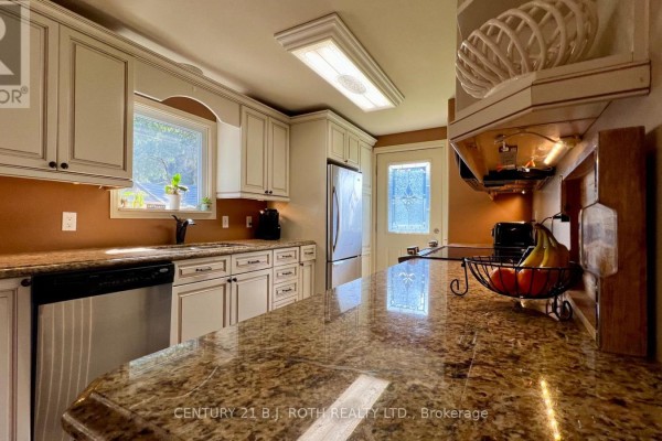 Long kitchen with white cabinets, granite countertops, stainless steel appliances, and a door. - 31 Corner Brook Trail, Innisfil