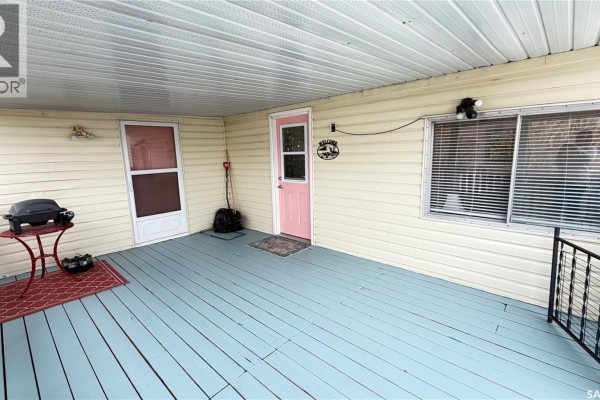 Covered deck of a mobile home with a pink door, screen door, window, and a small grill. - 31 Cypress Mobile Home Park, Maple Creek