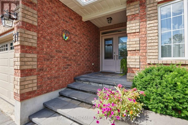 Front door with double glass panels and brick exterior, flanked by flower beds. - 31 Forillon Crescent, Ottawa