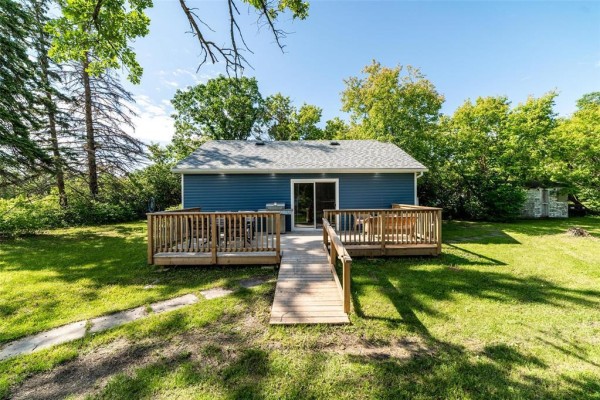 Rear view of the blue cottage, showing the wooden deck, ramp, and surrounding wooded area. - 31 Gimli Road, Dunnottar