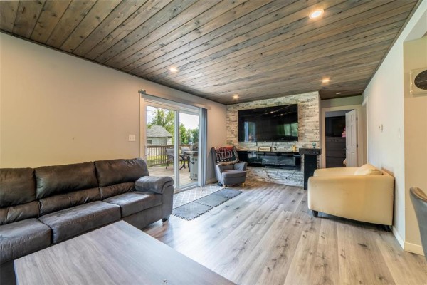 Living room featuring a large television mounted above a stone-covered fireplace, with sofas and an armchair. - 31 Gimli Road, Dunnottar