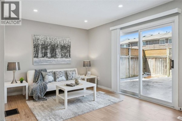 Living room with light wood floors, white sofa, coffee table, and sliding glass doors to a backyard. - 31 Greengate Road Unit# 239, Guelph