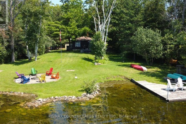 Aerial view of a waterfront property with a bungalow, fire pit, dock, kayaks, and canoes. - 31 Hillcrest Avenue, Kawartha Lakes