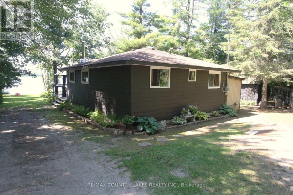 Side and rear exterior of the bungalow with a driveway, garden beds, and surrounding trees. - 31 Hillcrest Avenue, Kawartha Lakes