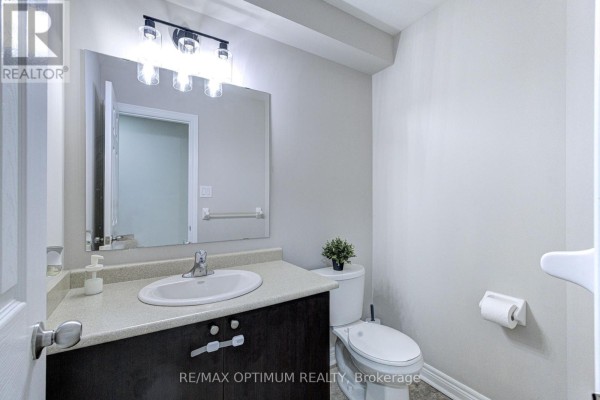 A small bathroom with a dark wood vanity, a white sink, a toilet, and a large mirror above the vanity. - 31 Keywood Street, Ajax