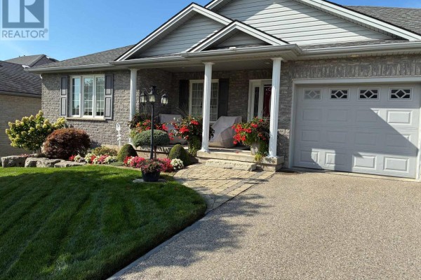 Front exterior of a brick house with a covered porch, garage, and manicured lawn. - 31 Morning Glory Drive, Tillsonburg