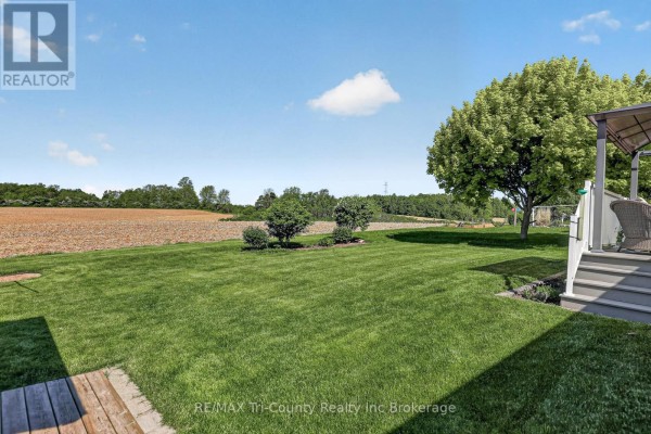 Backyard with green grass, trees, and a view of fields under a blue sky. - 31 Morning Glory Drive, Tillsonburg