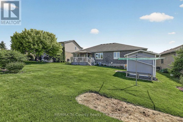 Rear view of a house with a green lawn, mature trees, and a fenced yard. - 31 Morning Glory Drive, Tillsonburg
