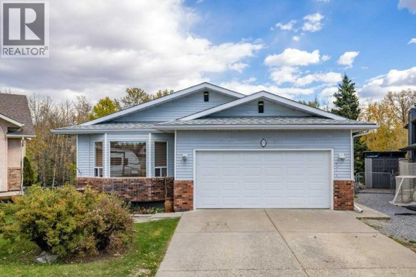 Front exterior of a light blue house with a white garage door, large windows, and a brick accent base. - 31 Riverside Place, Cochrane