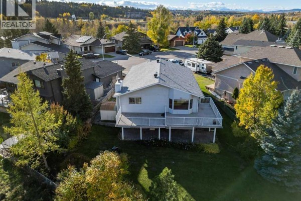 Rear aerial view of a white house with a substantial deck overlooking a treed lot and neighboring homes. - 31 Riverside Place, Cochrane