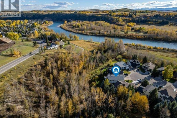 Aerial view of a residential neighborhood with homes surrounding a winding river and rolling, tree-covered hills. - 31 Riverside Place, Cochrane