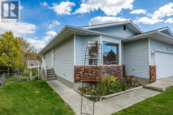 Side view of a light blue house showing a walkway, stairs to a side door, and a fenced backyard area. - 31 Riverside Place, Cochrane