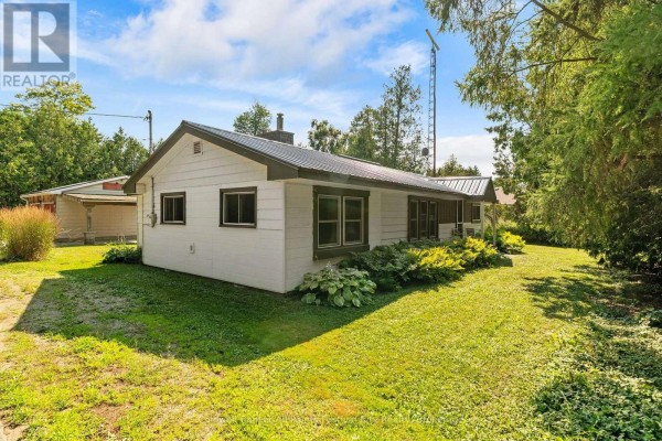 Side view of a white house with a metal roof and large windows, surrounded by green grass and landscaping. - 31 Salkeld Street, Central Huron