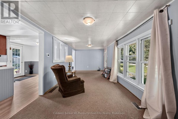 A carpeted sunroom with blue paneled walls, large windows with white curtains, and a brown armchair. - 31 Salkeld Street, Central Huron