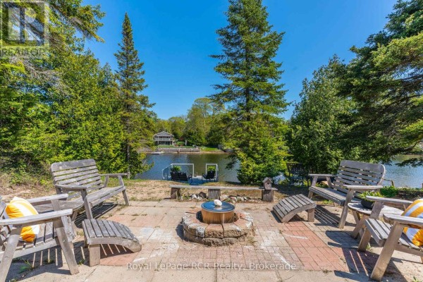 Outdoor seating area with fire pit and lake view, surrounded by trees. - 31 Sog-je-wa-sa Drive, Native Leased Lands