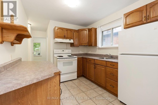 Kitchen with wood cabinets, white appliances, tiled floor, and laminate countertops. - 31 Thora Avenue, Toronto