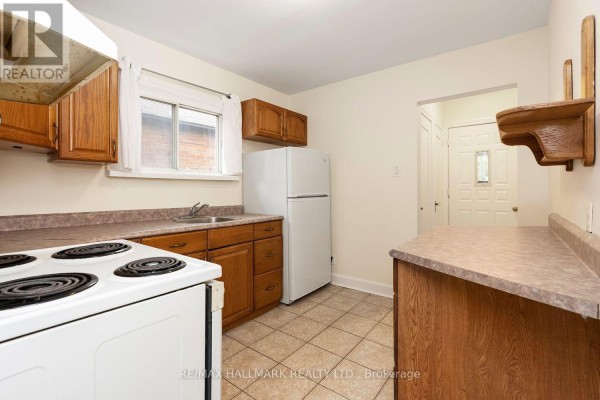 Kitchen with wood cabinets, white stove and refrigerator, tiled floor, and laminate counters. - 31 Thora Avenue, Toronto