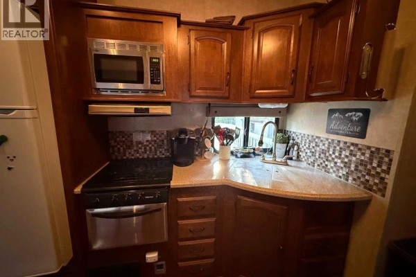 Fifth wheel kitchen with stainless steel appliances, wooden cabinets, and granite countertops. - 31 Timber Drive, 5230 27 Highway, Rural Mountain View County