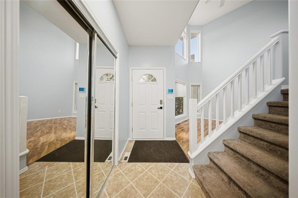 Entrance foyer with a white door, tiled floor, mirrored closet, and carpeted staircase. - 31 Treasure Cove, Winnipeg