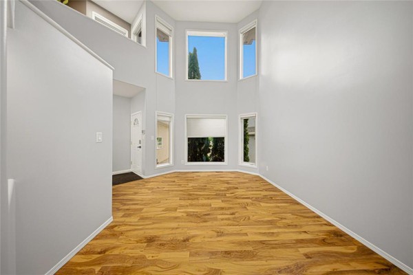 Empty living room area with large bay windows, light gray walls, and wood-look laminate flooring. - 31 Treasure Cove, Winnipeg
