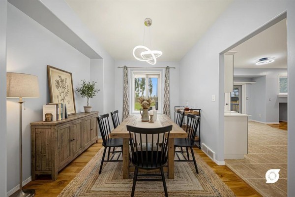 Dining room with a long wooden table, black chairs, buffet, and window overlooking a green field. - 31 Treasure Cove, Winnipeg