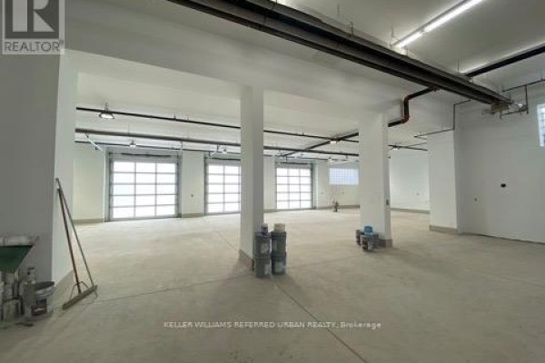Spacious interior of a commercial building with concrete floors, white walls, and multiple garage doors. - 31 Upton Road, Toronto