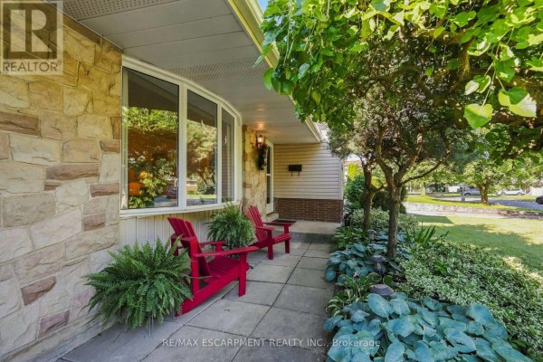 Front porch with light stone facade, bay window, two red chairs, and potted ferns. - 31 Valerie Drive, St  Catharines