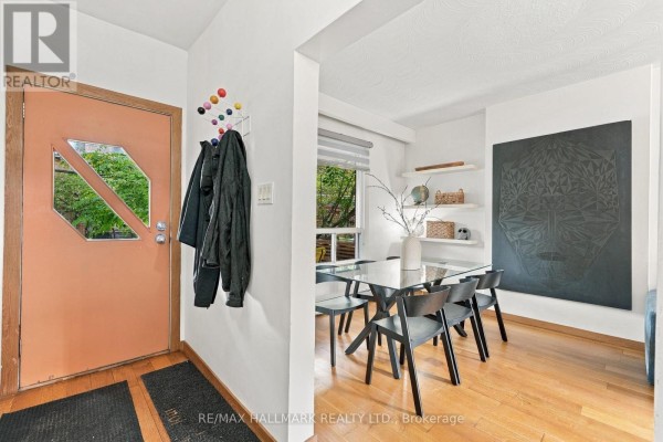 Interior entryway with an orange door, coats hanging, and a dining area with a glass table. - 31 Wright Avenue, Toronto