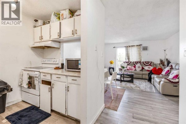 Kitchen with white cabinets and appliances, adjacent to a living room with a sectional sofa. - 310, 405 Columbia Boulevard W, Lethbridge