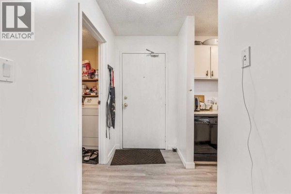 Interior hallway with a white front door, laundry closet, and view into the kitchen. - 310, 405 Columbia Boulevard W, Lethbridge