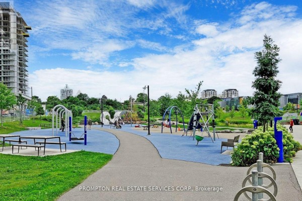 An outdoor playground with blue and grey rubberized surfacing, metal play structures, and green grass. - 310 - 115 Mcmahon Drive, Toronto
