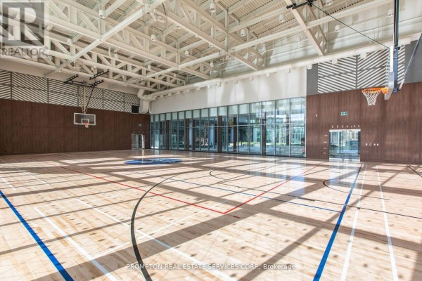 An indoor basketball court with a wooden floor, basketball hoops, and large glass windows. - 310 - 115 Mcmahon Drive, Toronto