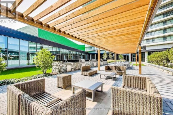 An outdoor patio with wicker furniture, metal tables, and a wooden pergola shading a seating area. - 310 - 115 Mcmahon Drive, Toronto