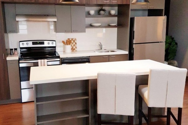 Modern kitchen with stainless steel appliances, grey and brown cabinets, and a white island with two stools. - 310 - 14 1/2 King Street E, Oshawa