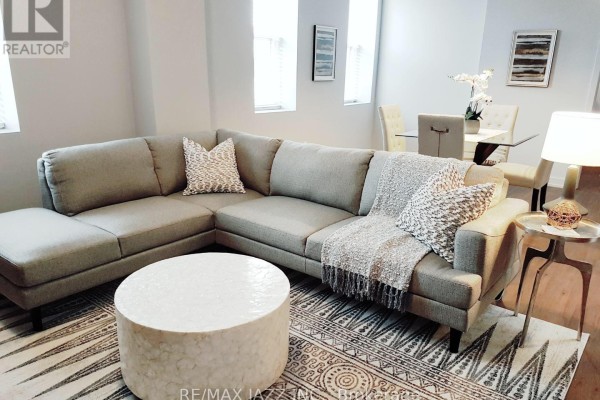 Living room with a large sectional sofa, patterned rug, coffee table, and a dining area in the background. - 310 - 14 1/2 King Street E, Oshawa