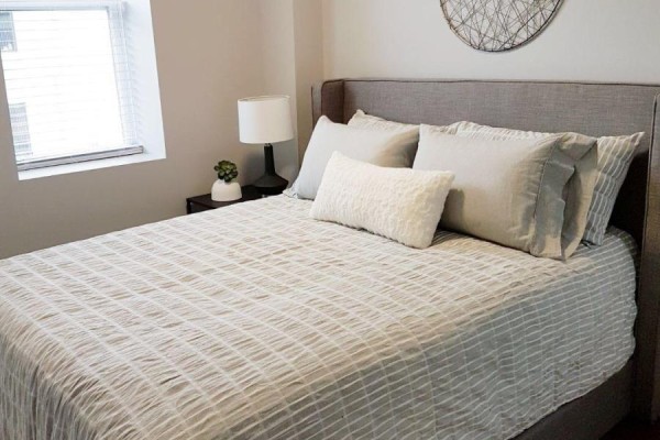 Bedroom with a king-size bed, grey headboard, light-colored bedding, and a bedside table with a lamp. - 310 - 14 1/2 King Street E, Oshawa