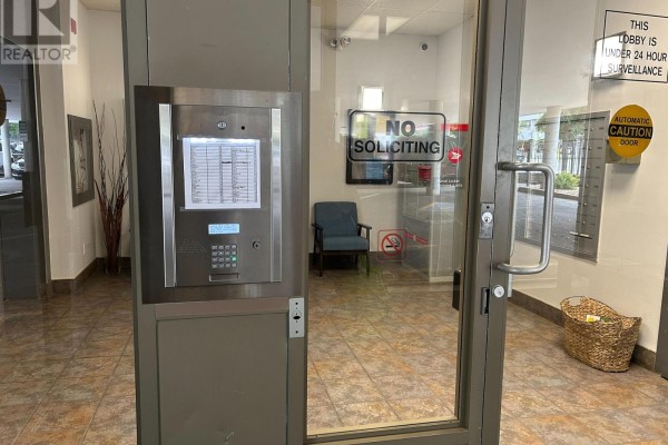 Building entrance with security intercom system, glass doors, and a waiting chair. - 310 - 160 Wellington Street E, Aurora
