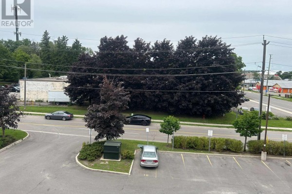 View from apartment window showing parking lot, street, and dark-leaved trees. - 310 - 160 Wellington Street E, Aurora