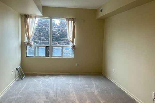 Empty bedroom with beige carpet, pale yellow walls, and a large window with curtains. - 310 - 160 Wellington Street E, Aurora