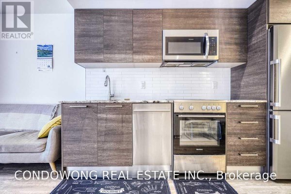 Close-up of the kitchen area featuring stainless steel appliances, granite countertops, and white subway tile backsplash. - 310 - 28 Wellesley Street E, Toronto