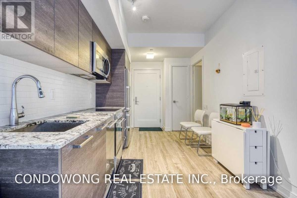 View of the apartment entrance and kitchen with light wood flooring, white walls, and contemporary cabinetry. - 310 - 28 Wellesley Street E, Toronto