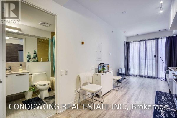 View of the bathroom with a toilet, sink, and shower, adjacent to the living area with wood flooring. - 310 - 28 Wellesley Street E, Toronto