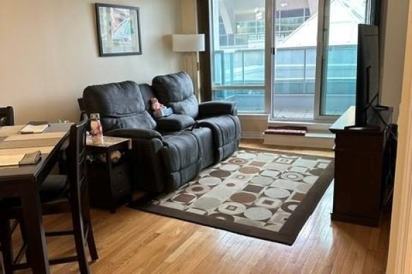 Living area with dark gray sofa, dining table, wood floor, and large window with view. - 310 - 33 Elm Drive, Mississauga