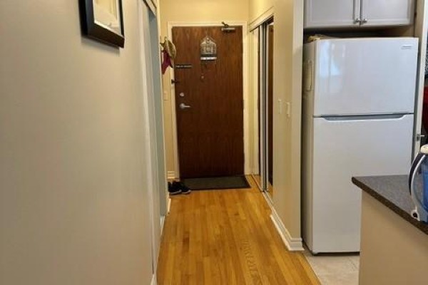 Hallway with light beige walls, wood floor, brown door, and white refrigerator on the right. - 310 - 33 Elm Drive, Mississauga
