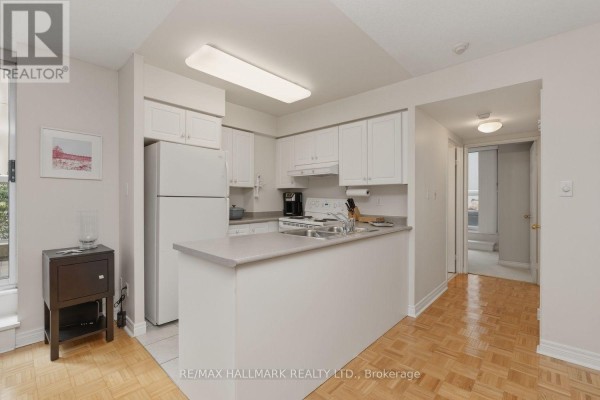 White kitchen with a refrigerator, stove, sink, and a breakfast bar, with a view of a hallway. - 310 - 43 Eglinton Avenue E, Toronto