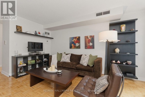 Living room showing a sofa, armchair, media console, artwork, and shelving units. - 310 - 43 Eglinton Avenue E, Toronto